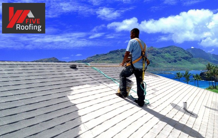 Worker applying reflective coating on a roof to reduce energy costs.